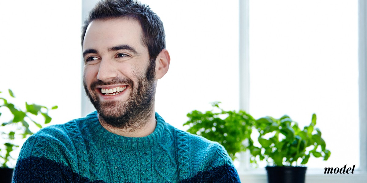 Male Model in Turquoise Sweater Smiling In Front of Window